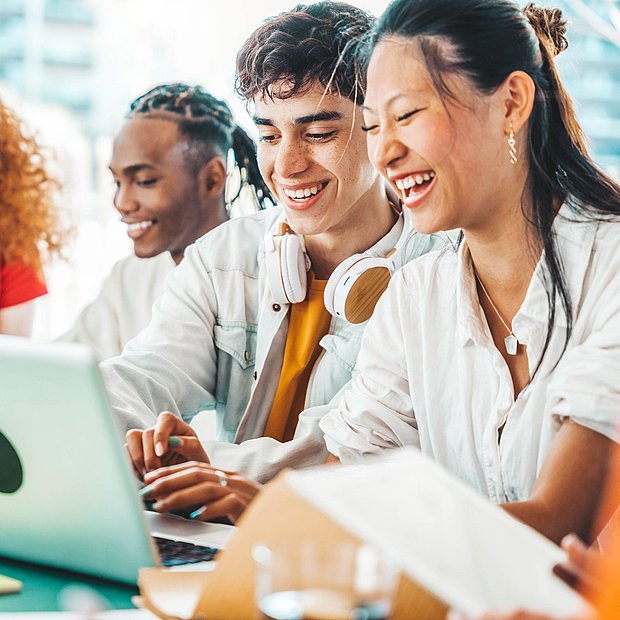 Unterschiedliche Studenten sitzen zusammen und nehmen an einem Laptop an einer Online-Vorlesung teil.